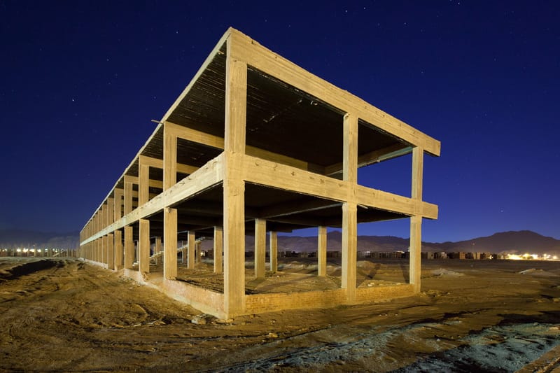 Skeleton of an unfinished concrete building under a deep blue night sky, Egyptian desert hills behind