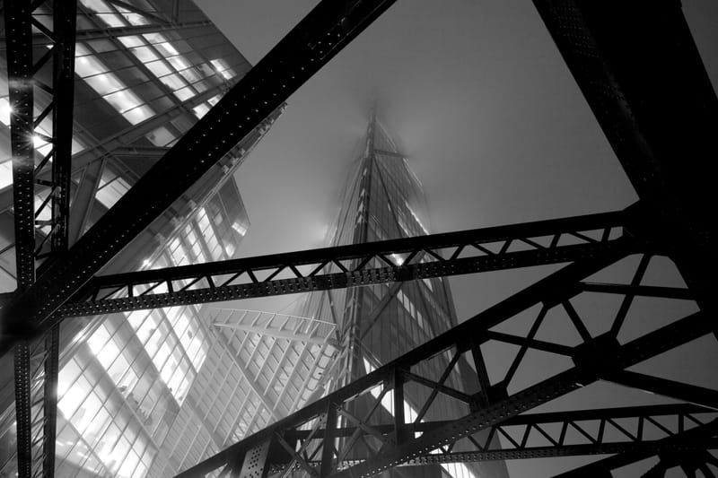 Black and white view up through riveted steel girders to a fog-lit building beyond, Worship Street, Shoreditch