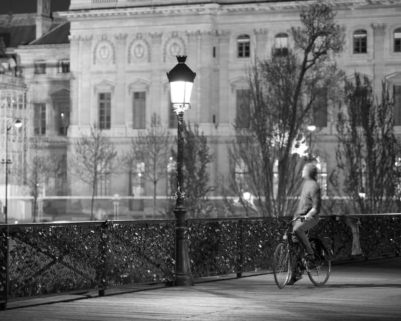 Cyclist crossing the Pont des Arts past an ornate lamppost at night, Paris