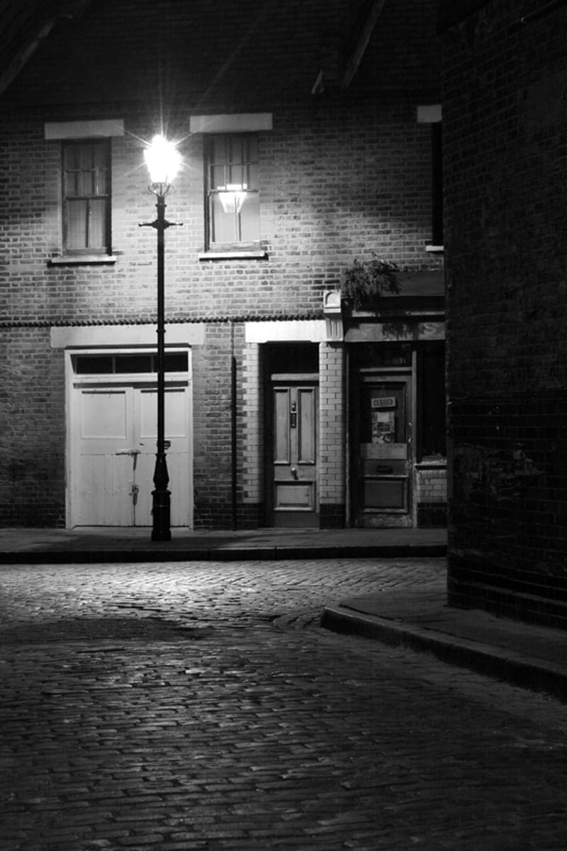 Street lamp lighting a brick corner house on the cobbles of Ezra Street, East London, at night
