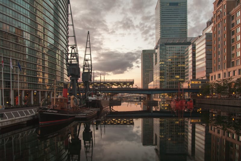 Dock cranes and moored barges below Canary Wharf towers at sunrise