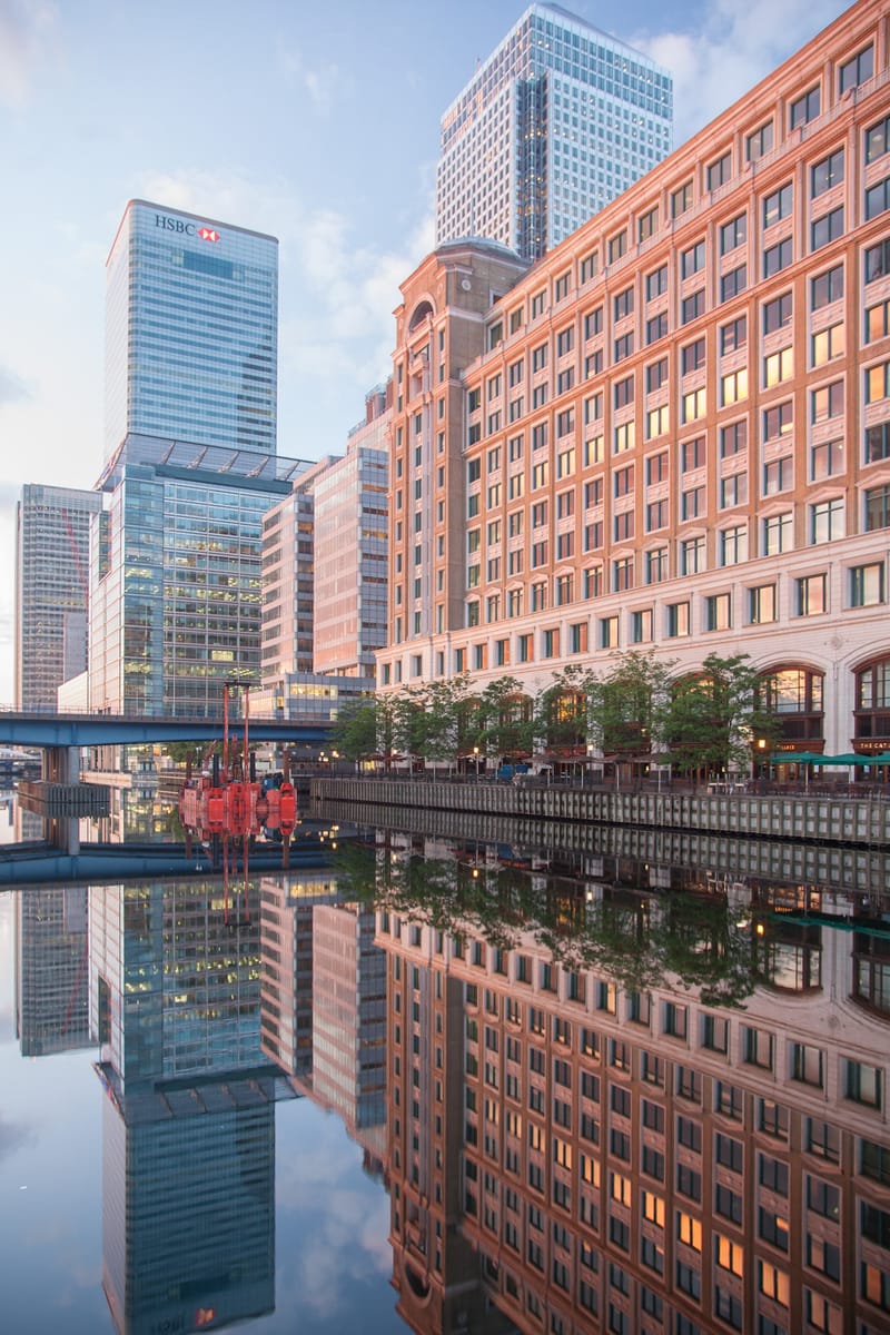 Brick warehouse and glass towers reflected in the dock at sunrise