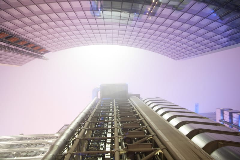 The Lloyd's building's lift towers vanishing into violet fog, seen from below