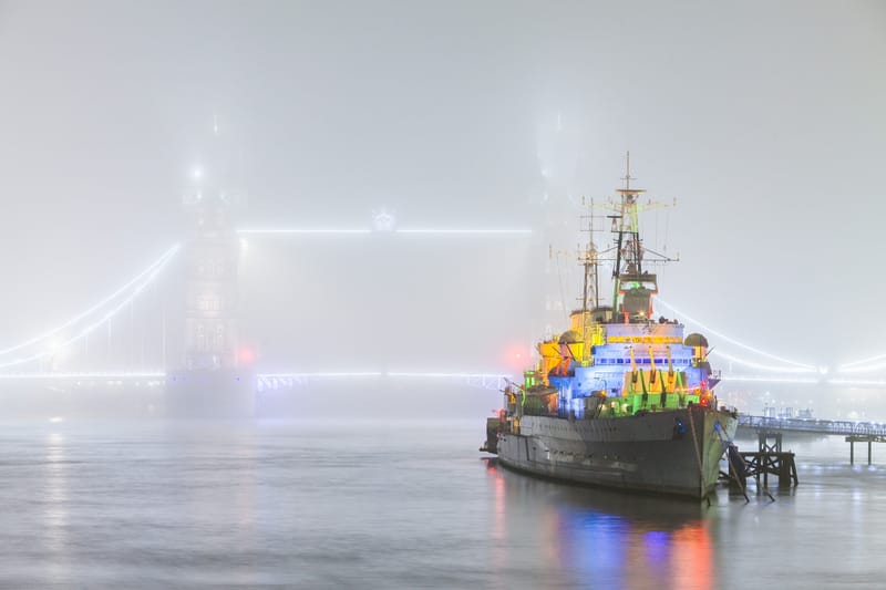 HMS Belfast dressed in coloured lights on a foggy Thames, Tower Bridge outlined behind