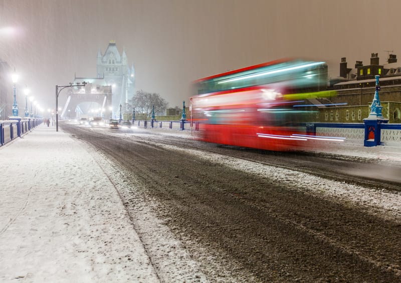 A red London bus blurring through snow on the Tower Bridge approach at night