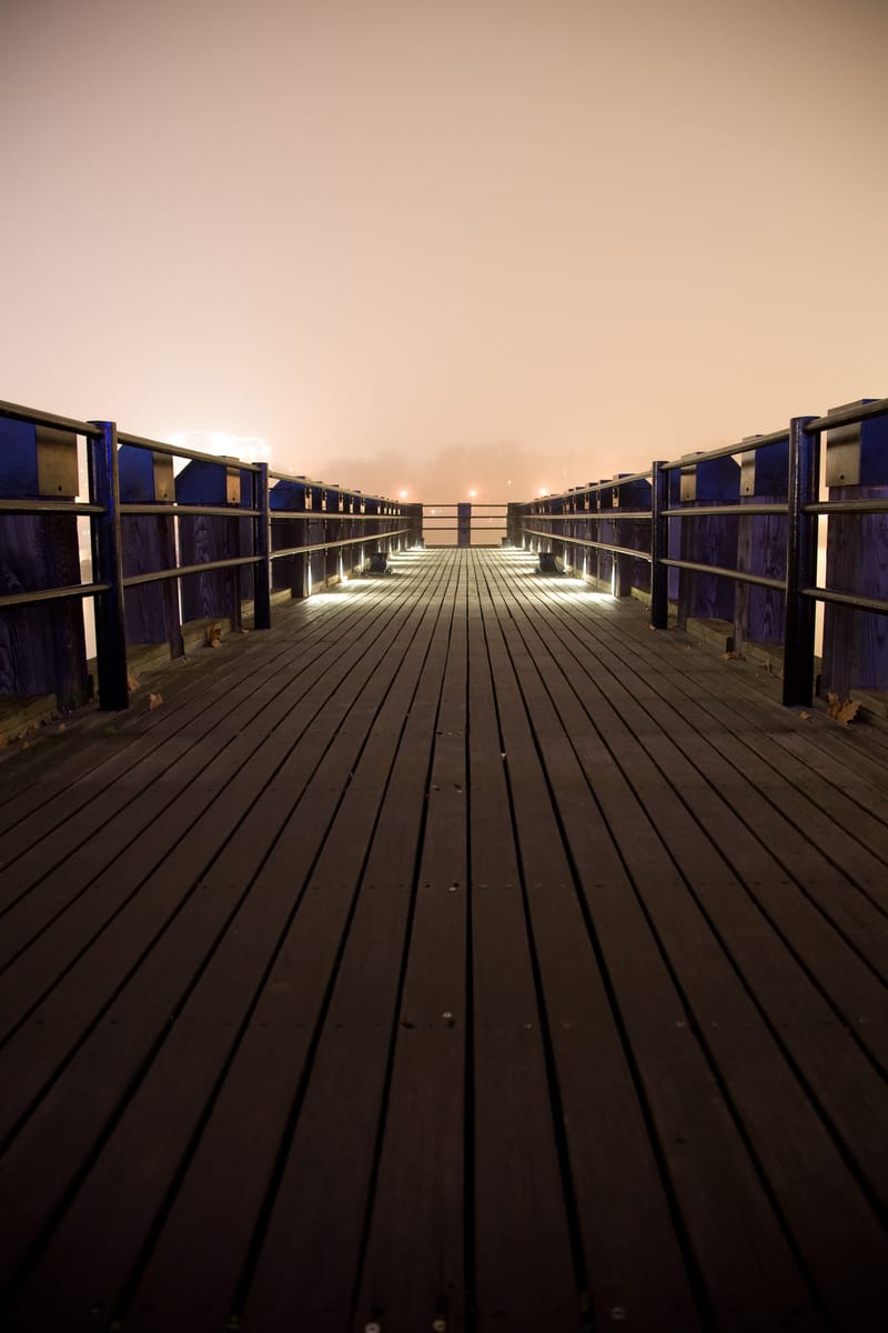 Empty wooden pier leading into glowing fog on the Thames at night — Oxo Tower pier