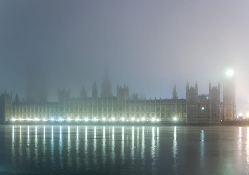 The Houses of Parliament floodlit across the Thames in mist, lights reflected in the river