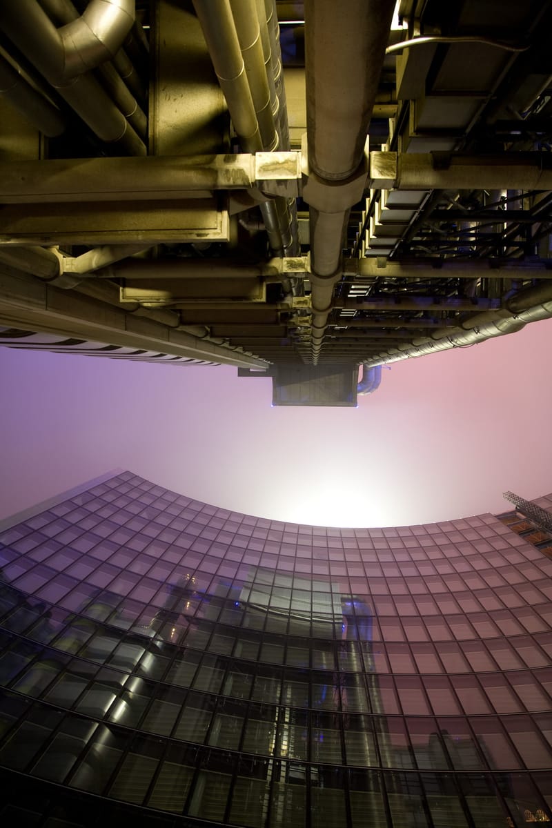 Pipework of the Lloyd's building overhead, a curved glass tower rising into fog beyond