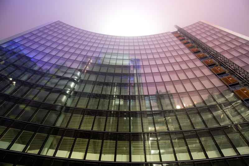 Curved glass office façade rising into glowing fog at night, City of London