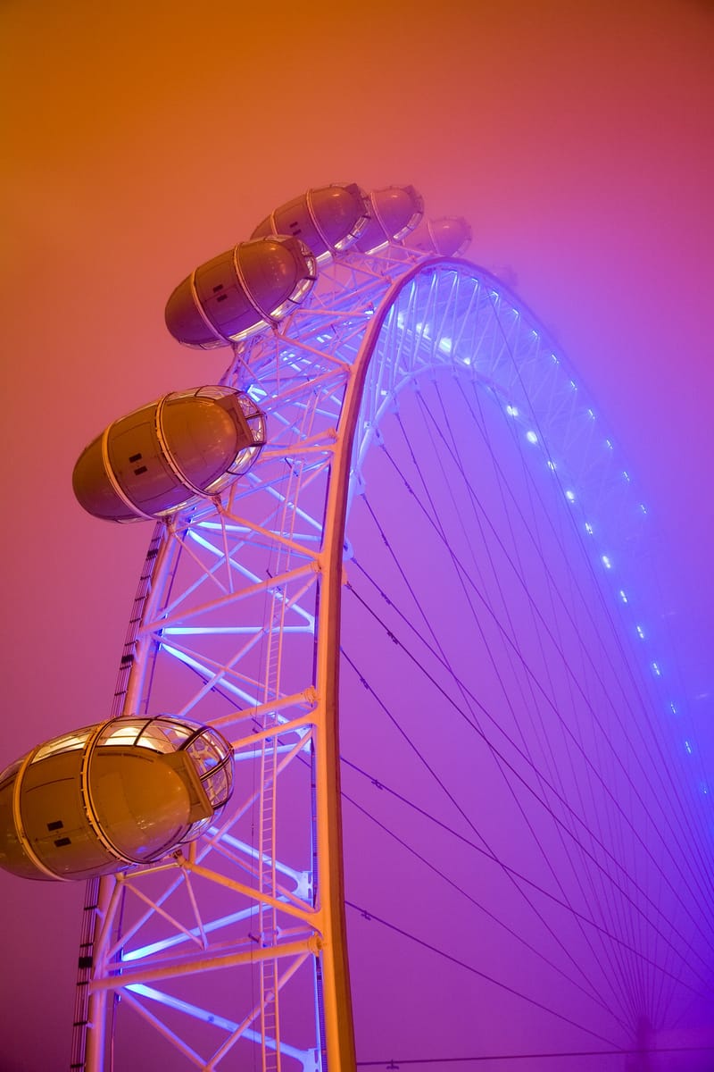 The rim and capsules of the London Eye lit violet in fog