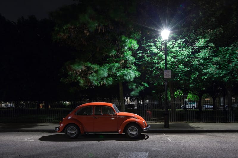 A red Volkswagen Beetle parked beneath lamplit trees at night, London