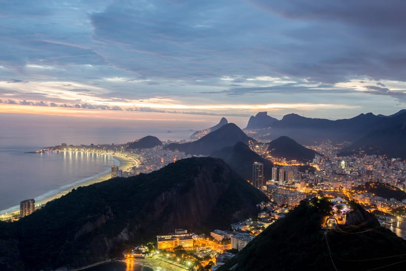 Copacabana curving below wooded hills at dusk, city lights coming on, Rio de Janeiro
