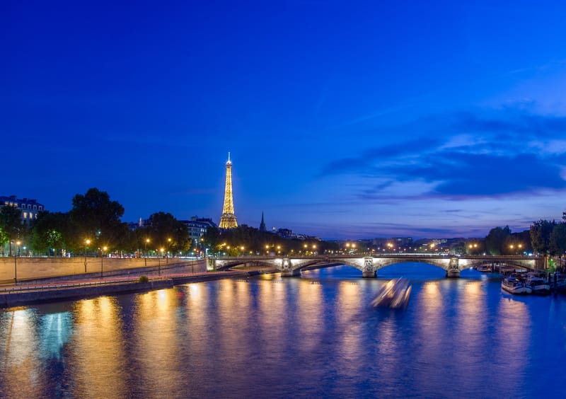 The Eiffel Tower lit at dusk beyond a lamplit bridge over the Seine