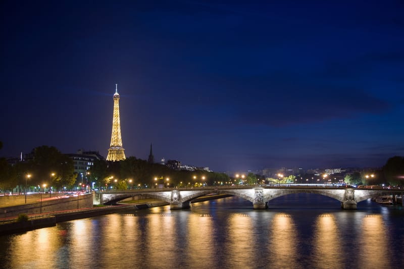 The Eiffel Tower glowing above a bridge on the Seine at night, lights reflected in the river