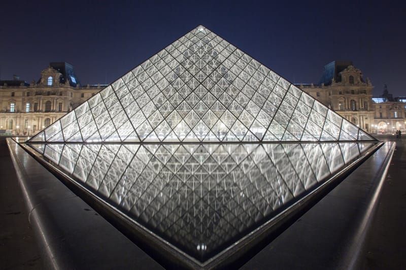 The Louvre pyramid glowing at night between the palace wings