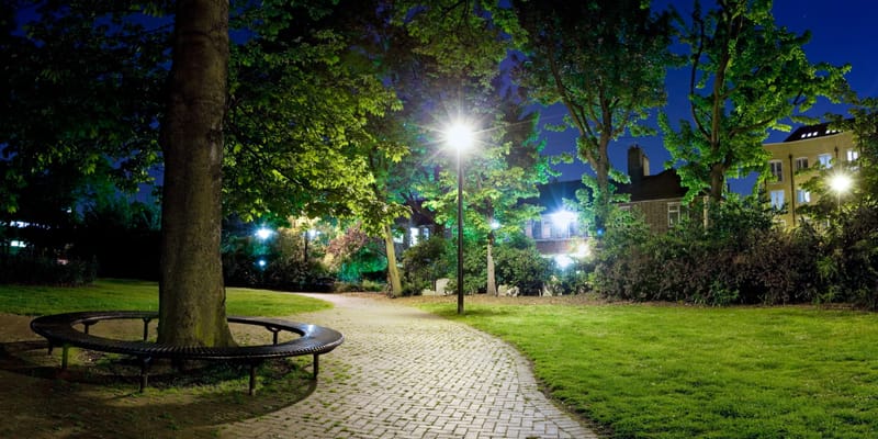 A circular bench around a tree trunk on a cobbled clearing at night