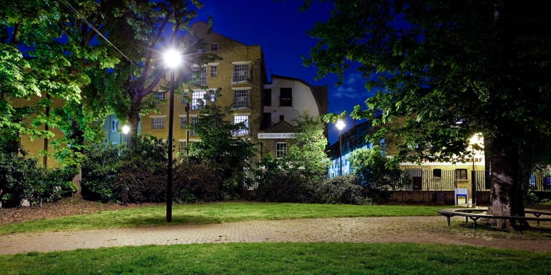 A lamplit green with a curving path and cottages beyond at night