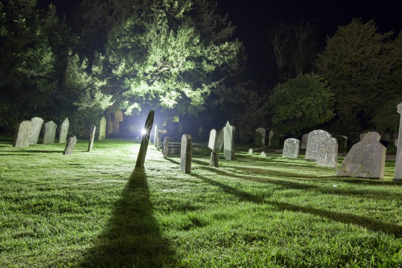 Gravestones in lamplight, long shadows across frosted grass at night