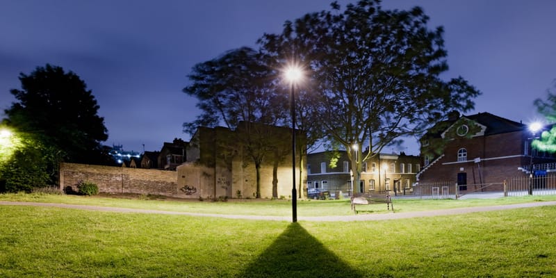 Floodlit lawn and an old brick wall at night, houses beyond