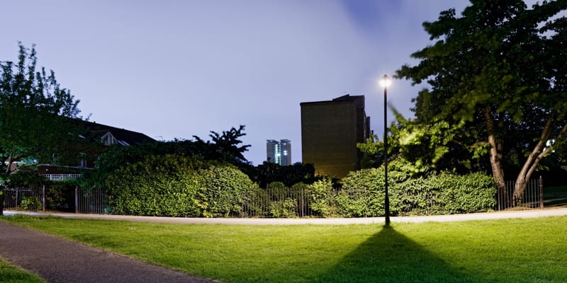 A streetlamp casting its shadow across a park lawn at night, tower blocks beyond