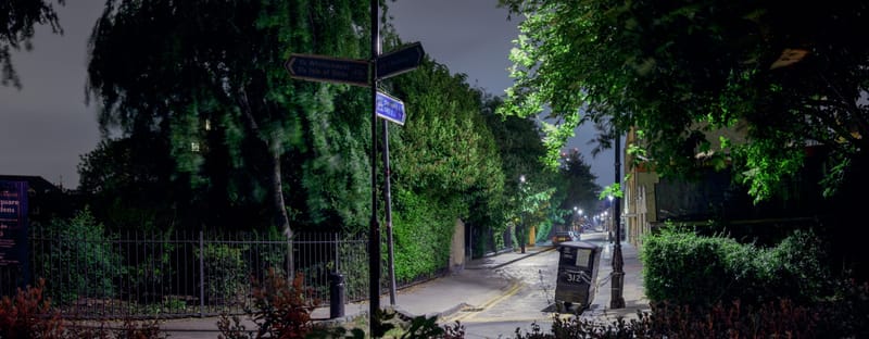 Park gateway and noticeboard under lamplight at night, a lane fading into darkness
