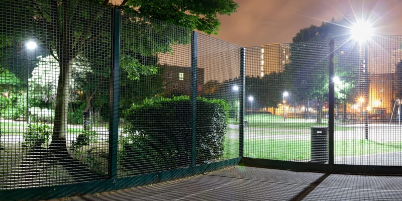 Night panorama through the mesh of a games court, trees and tower blocks beyond