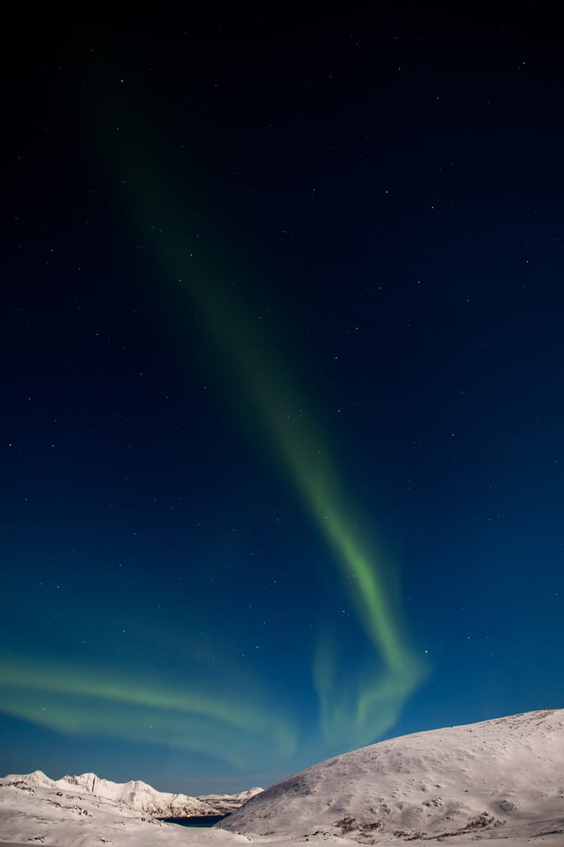 A green arc of the northern lights over a snow-covered ridge, Tromsø, Norway
