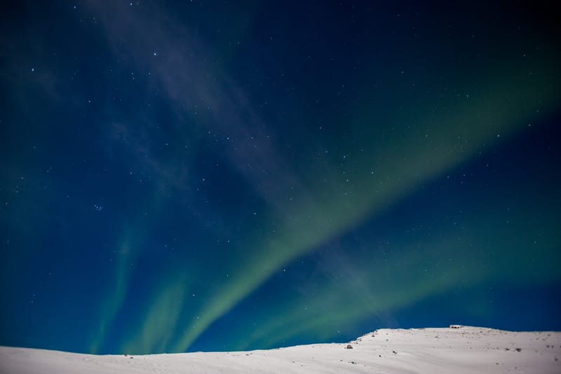 The northern lights rippling above snowy hills under a starry sky, Tromsø, Norway