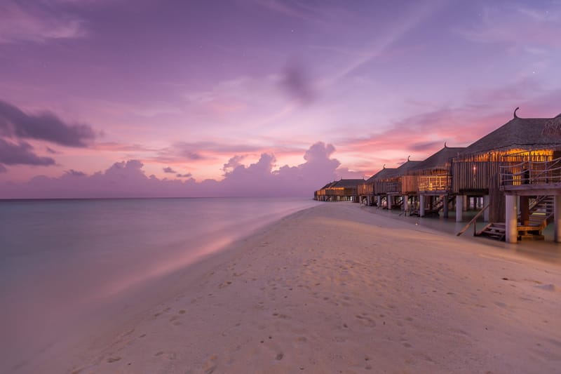 Overwater villas at the end of a sand spit under a violet dusk sky, Maldives