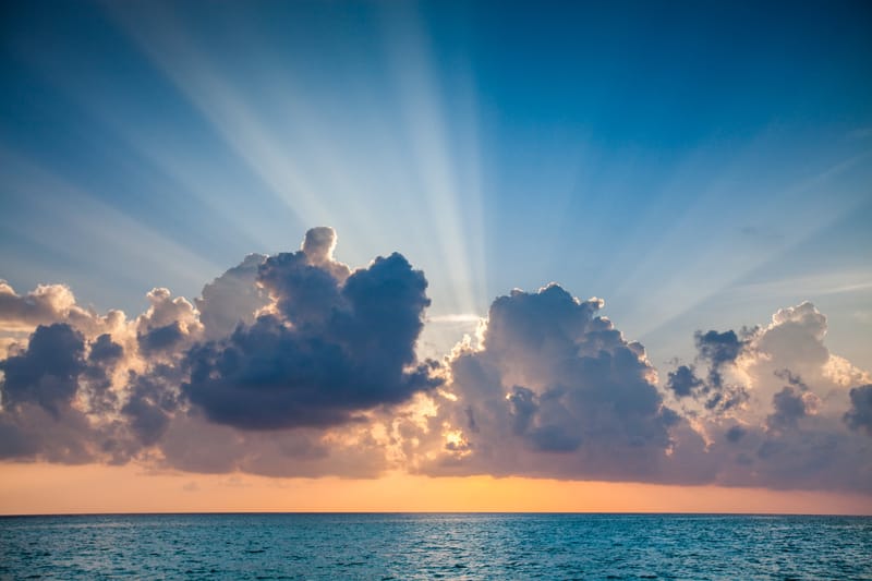 Sunbeams bursting from behind a dark cloud over the sea