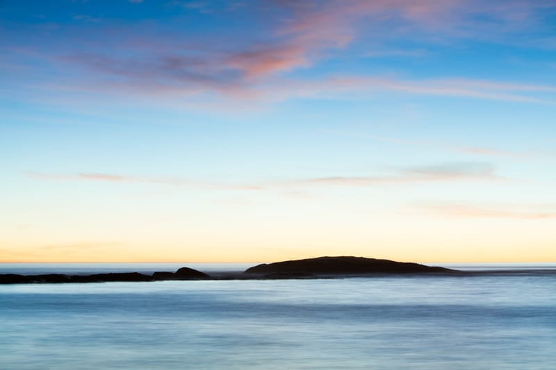 An island on the horizon under a pastel dusk, long-exposure water