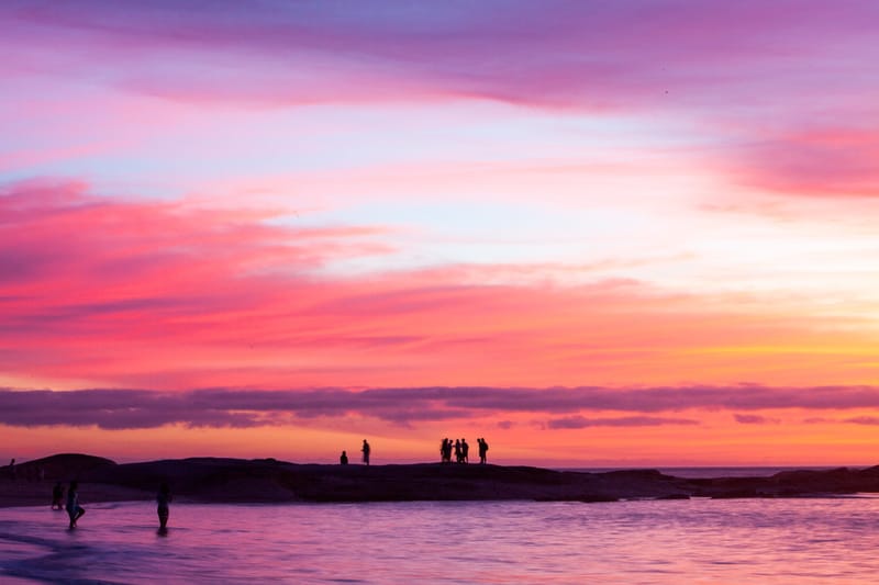 Bathers silhouetted on shoreline rocks under a vivid pink sunset, Rio de Janeiro