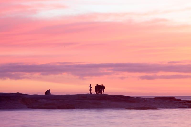 A small group silhouetted on a sea rock under layered pink clouds at dusk, Rio de Janeiro